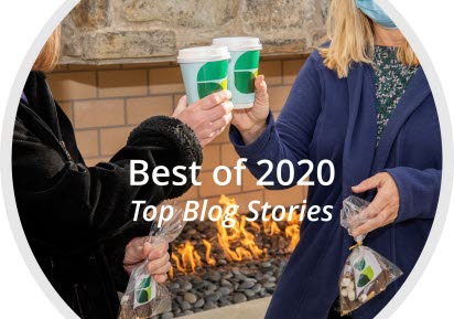 Two women toast with coffee cups in front of a fireplace